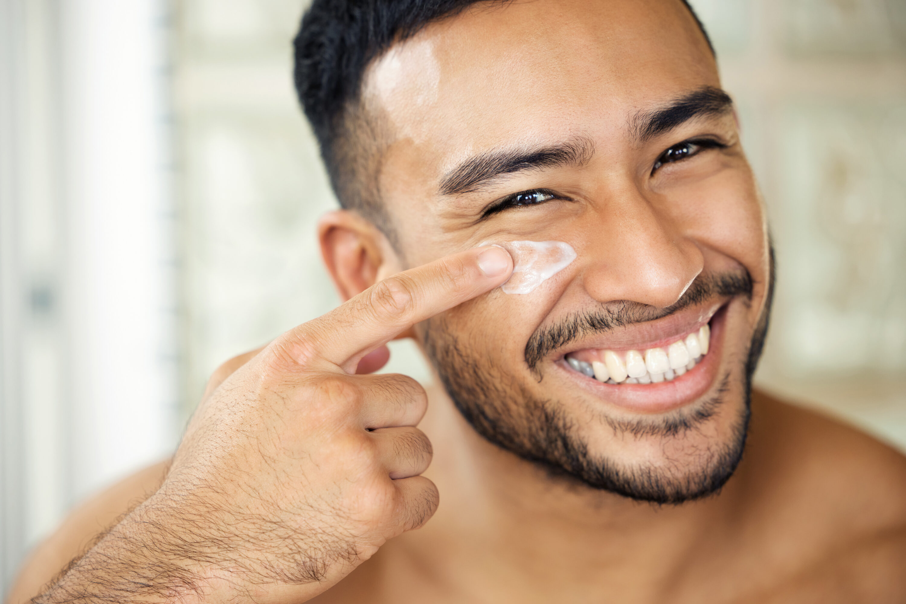 Man, bathroom and skincare with moisture, portrait and smile for health, cosmetics and self care in morning. Indian guy, skin wellness and youth for natural glow, cream and happiness with routine.